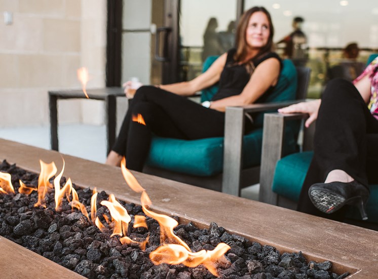 two women sitting oudoors in lounge chairs around a fire pit table